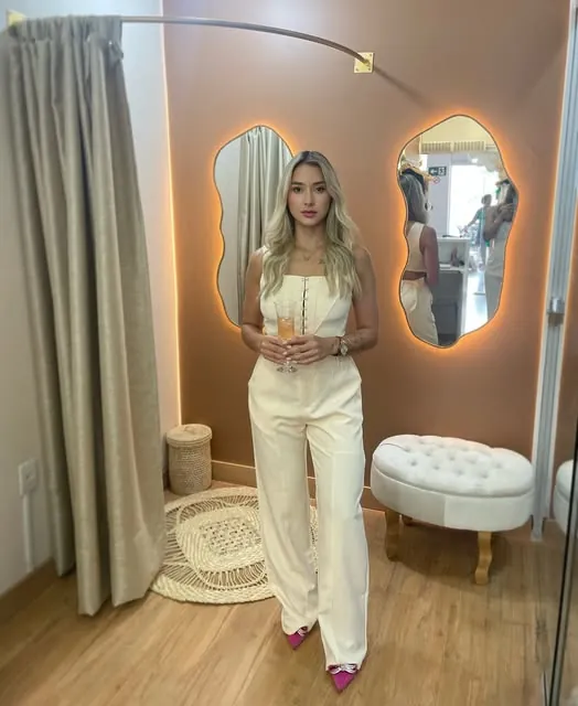 Giovana Santiago de conjunto claro, diante de dois espelhos orgânicos com luz quente